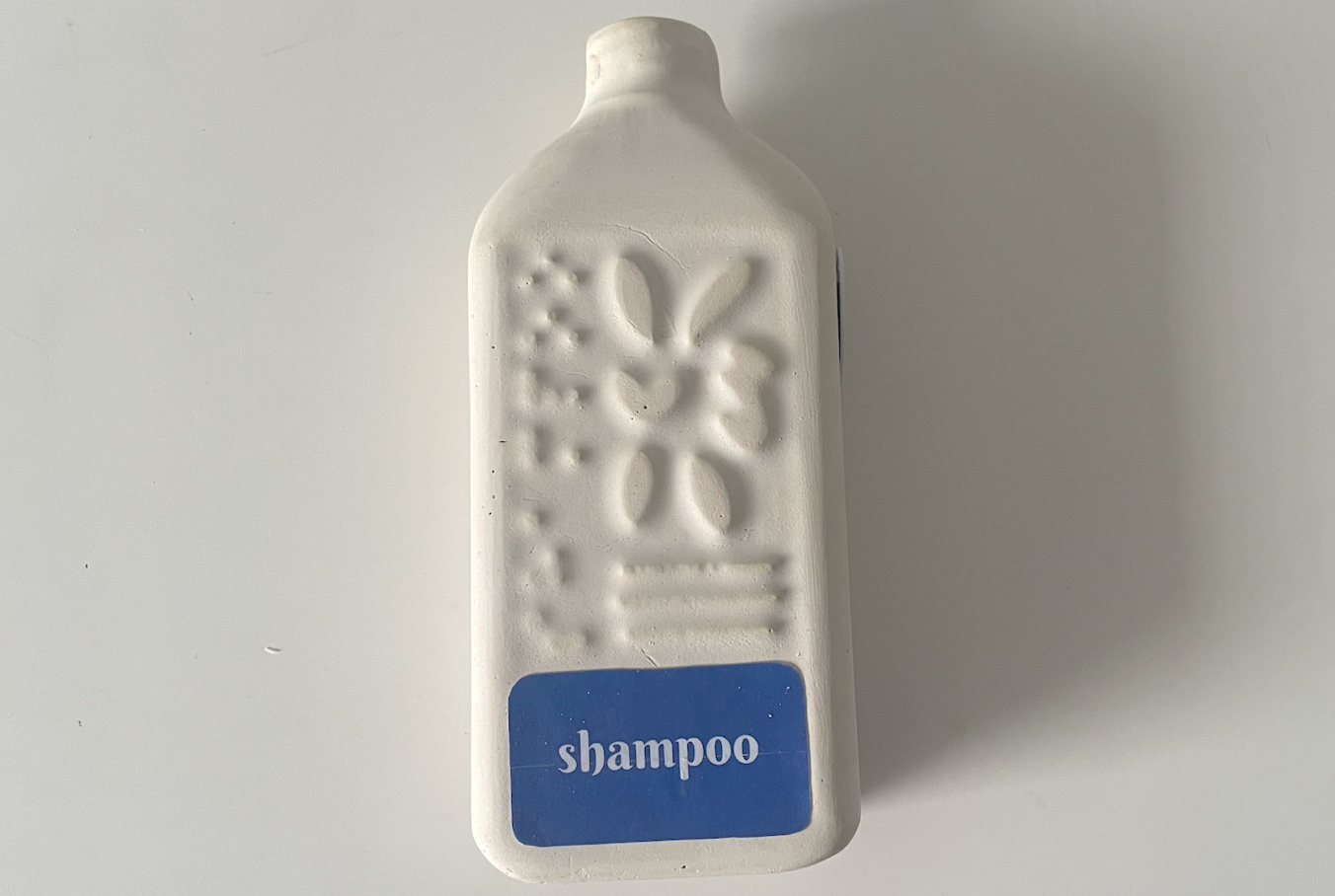 Plaster cast of a Flower Form shampoo bottle with an NFC tag on the side and a blue label on the front
